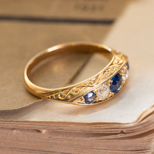 A Victorian five stone ring with blue sapphires and diamonds set in yellow gold with intricate engraved scroll details.