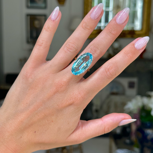 aquamarine and yellow gold cocktail ring on left hand, middle finger. Photographed with hand held up and antiquated bokeh background. 