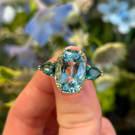 Aquamarine and teal tourmaline three-stone large cocktail ring held in between fingers showing detail
