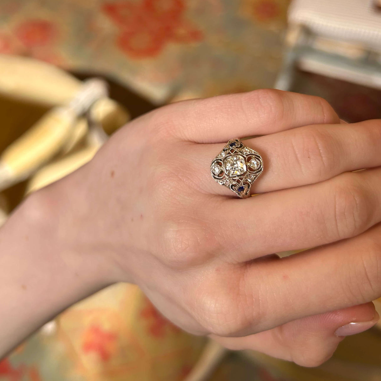 Relaxed hand held up to see details of diamond and sapphire cluster ring