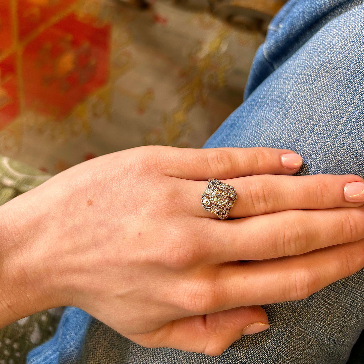Hand wearing art deco diamond and sapphire intricate cluster ring in relaxed position against jeans