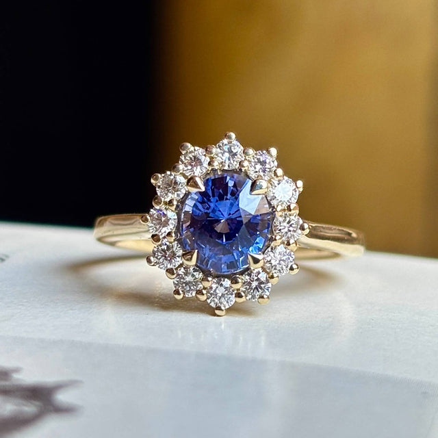 Blue sapphire and diamond cluster engagement ring, close-up on light surface showing fine details.