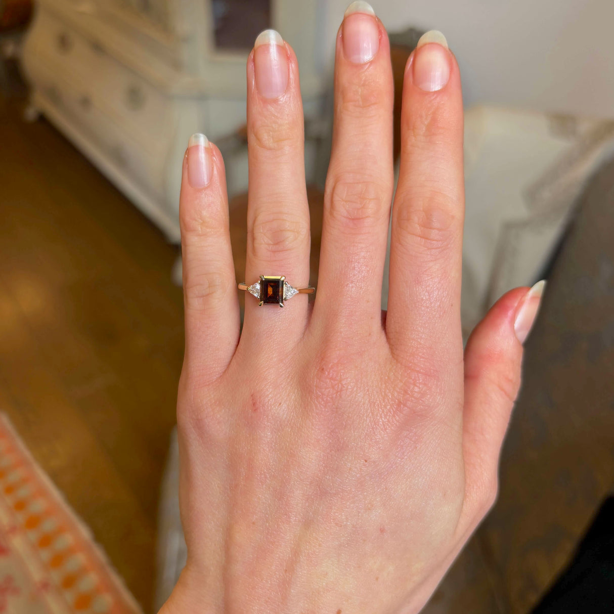 Brown diamond three-stone engagement ring on hand from a. distance showing scale