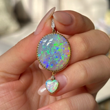 Cabochon opal pendant, held in fingers.