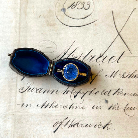 Blue sapphire round solitaire gold ring in an open ring box with a background of antique paper