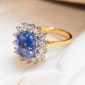 An antique inspired, gold engagement ring with a Ceylon blue sapphire with a diamond cluster.