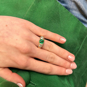 Emerald and diamond trilogy ring worn on hand against a green fabric background