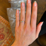 Round cut and pear-cut diamond three-stone yellow gold engagement ring on hand. 