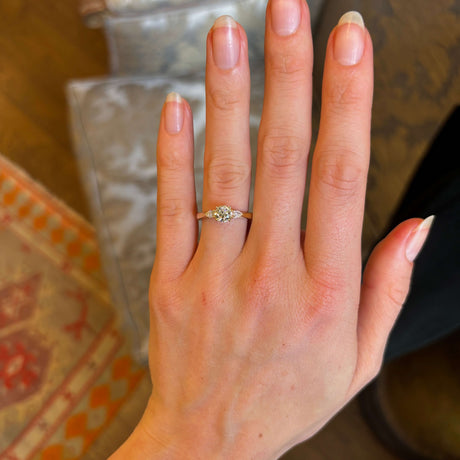Round cut and pear-cut diamond three-stone yellow gold engagement ring on hand. 