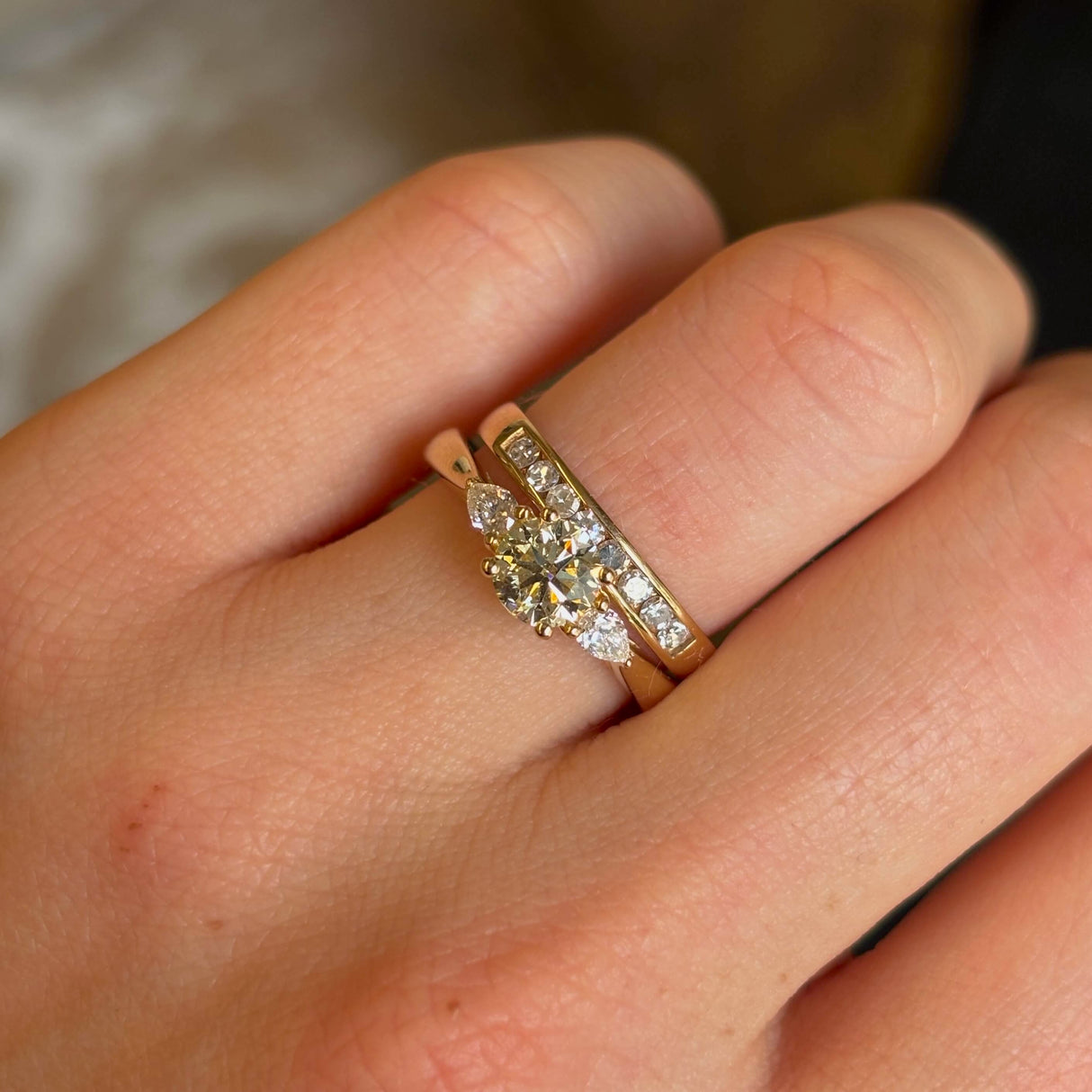 Round-cut and pear-cut diamond three-stone yellow gold engagement ring close up on hand paired with a wedding band. 