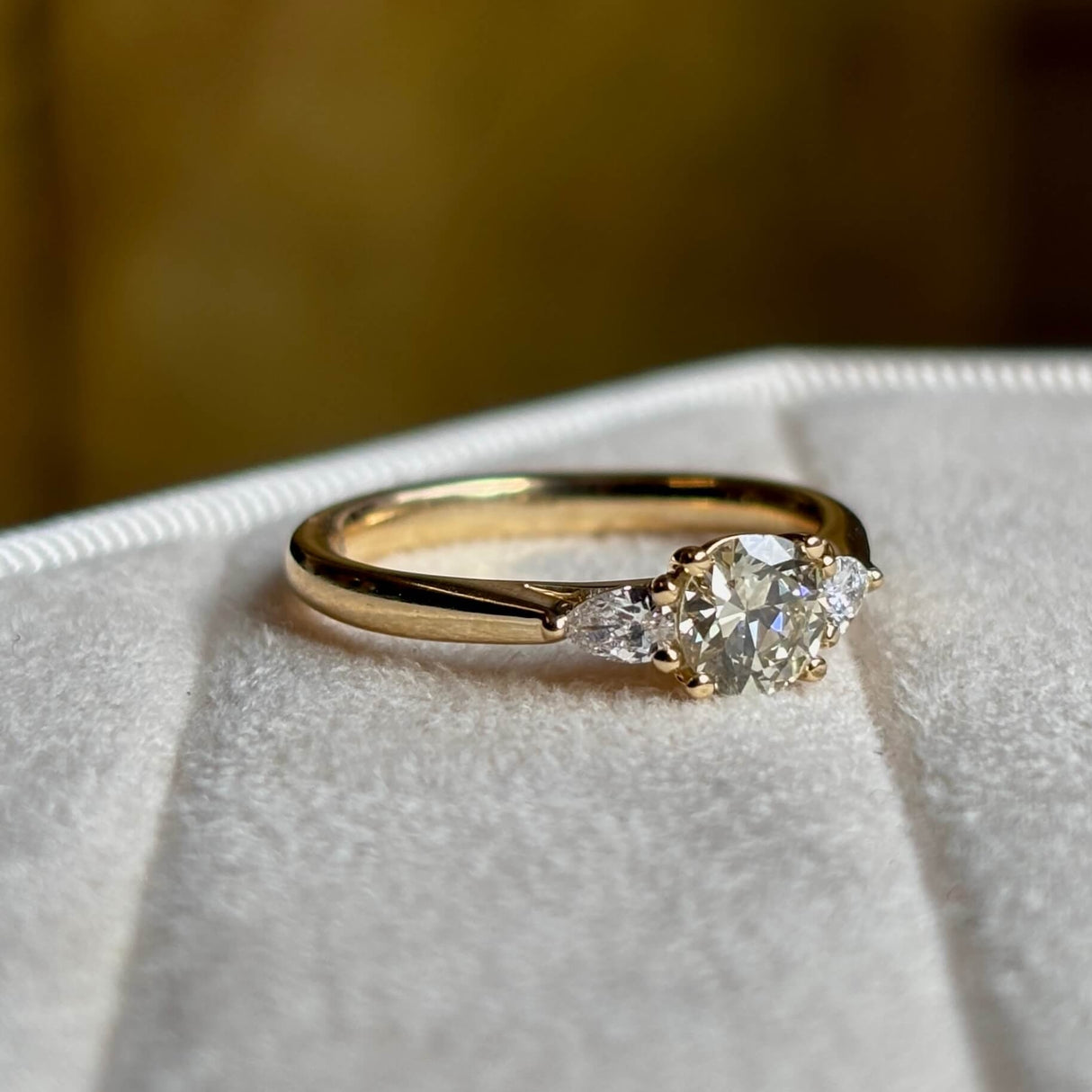 Diamond three-stone engagement ring angled side on showing pear-cut secondary diamonds and band. 