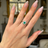 Edwardian emerald and diamond cluster ring worn on hand.