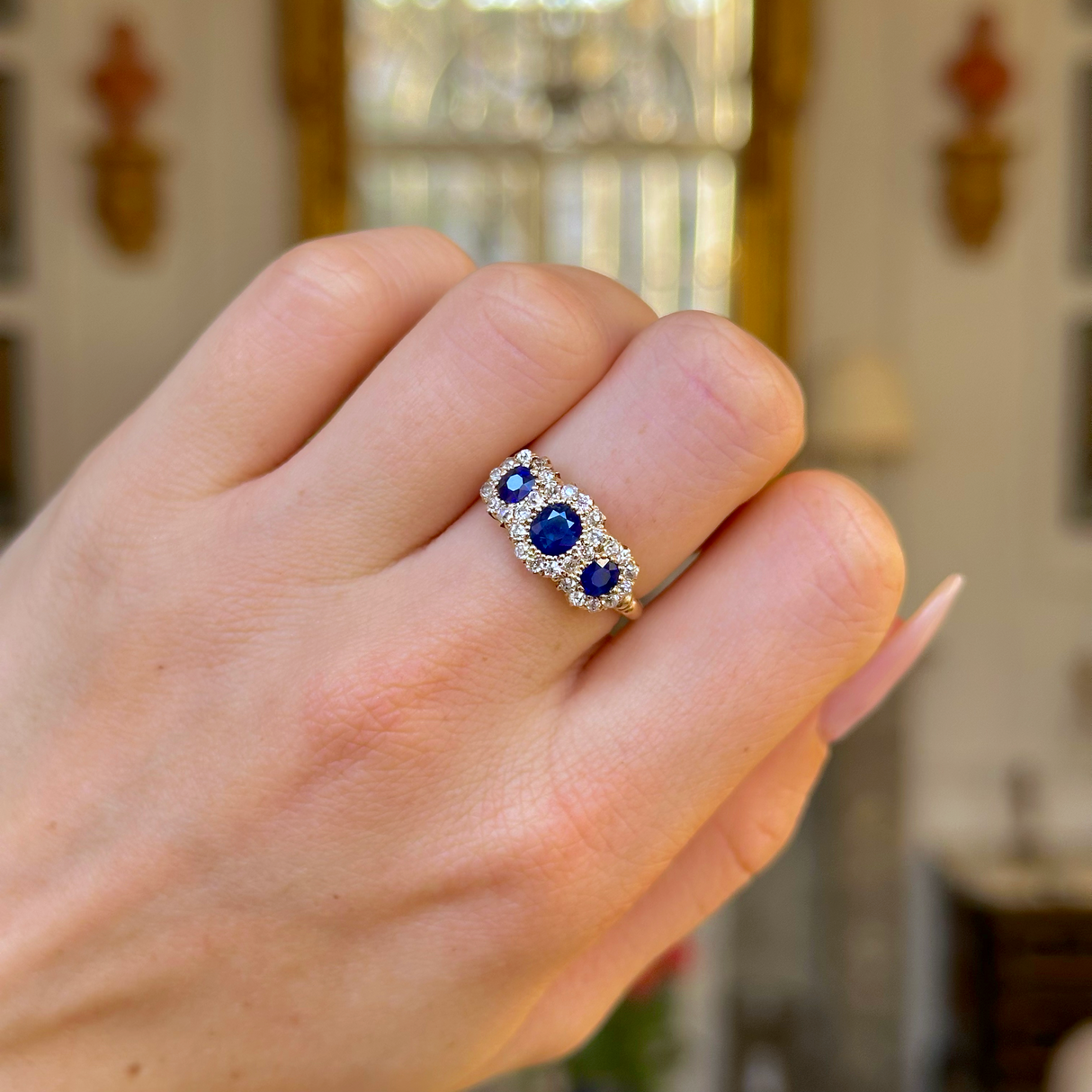 sapphire and diamond triple cluster ring worn on closed hand.