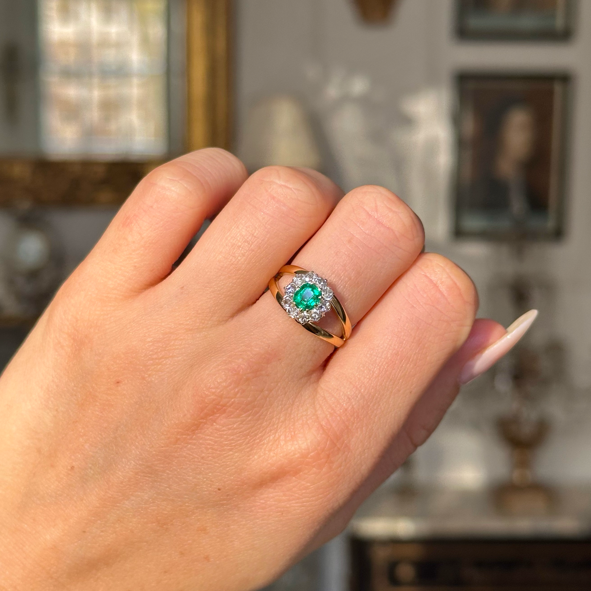 Vintage emerald and diamond cluster ring on closed hand. 
