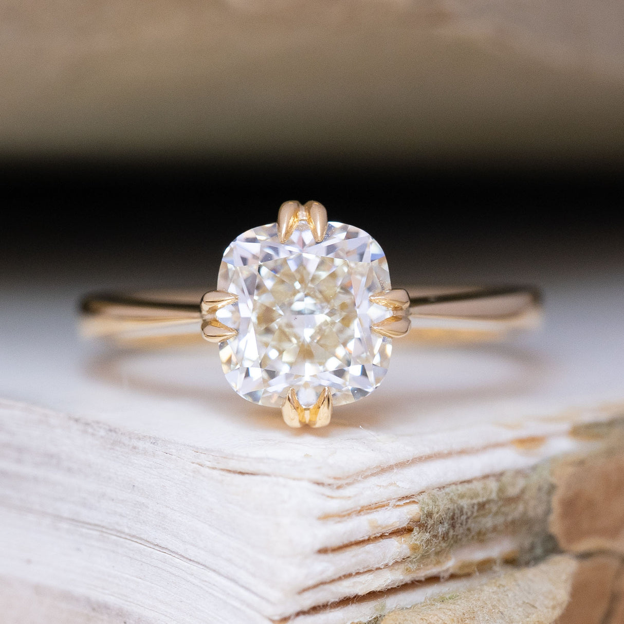 An antique-inspired, warm toned cushion-cut diamond solitaire ring in yellow gold.