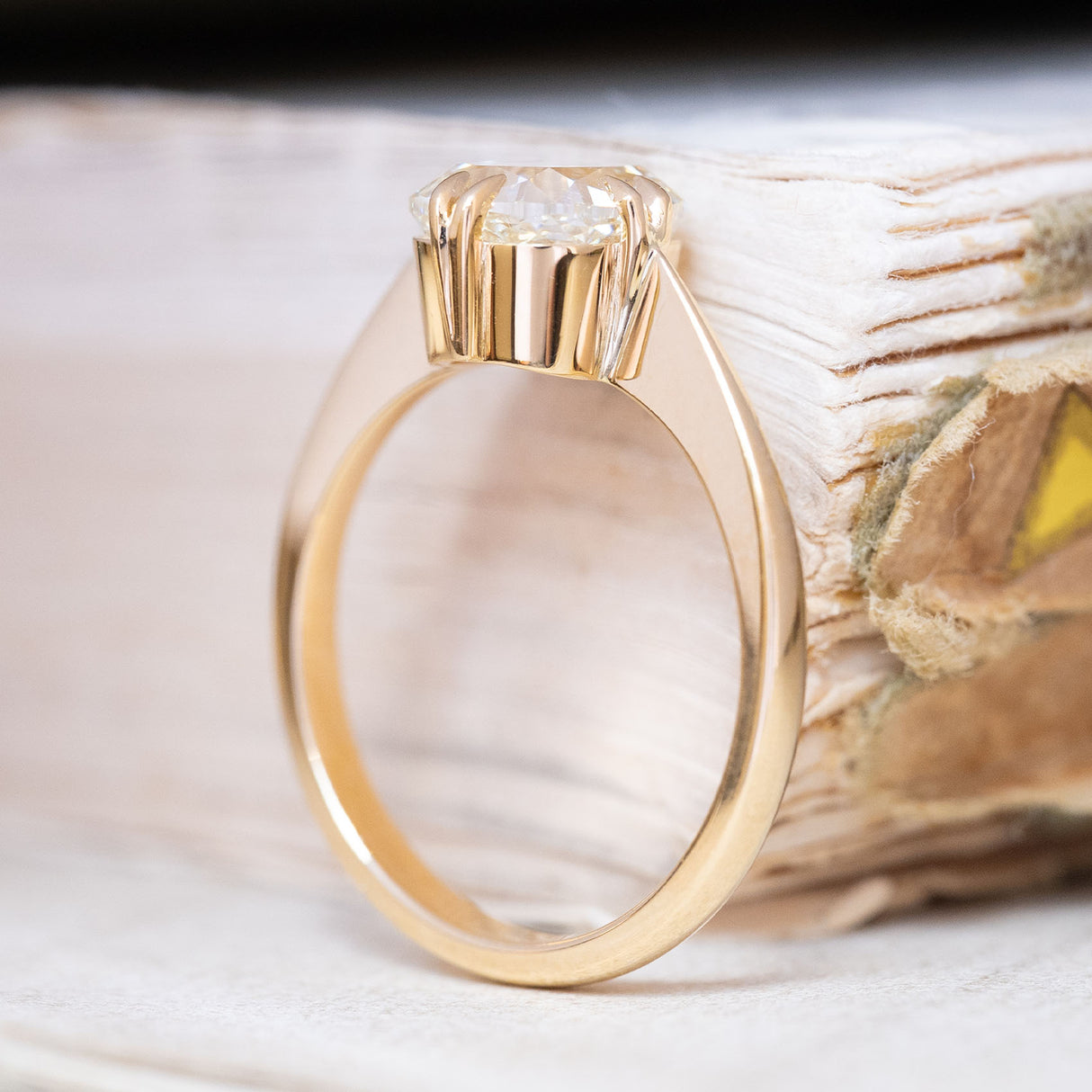 An antique-inspired, cushion-cut diamond solitaire ring in yellow gold displayed upright. 