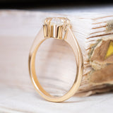 An antique-inspired, cushion-cut diamond solitaire ring in yellow gold displayed upright. 