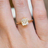 An antique-inspired yellow-toned cushion-cut diamond solitaire ring in yellow gold worn on the finger.