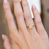 An antique-inspired yellow-toned cushion-cut diamond solitaire ring in yellow gold worn on the hand.