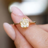 An antique-inspired yellow-toned cushion-cut diamond solitaire ring in yellow gold held between the fingers.