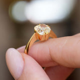 Side detail of an antique-inspired yellow-toned cushion-cut diamond solitaire ring in yellow gold held between the fingers.