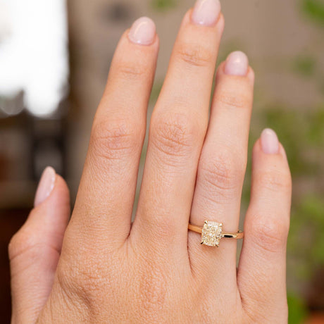A hand wearing an Antique-inspired, cushion-cut diamond solitaire engagement ring in yellow gold 