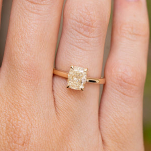 A close-up of a yellow gold antique-style ring with a cushion-cut diamond claw-set and worn on a person's finger.