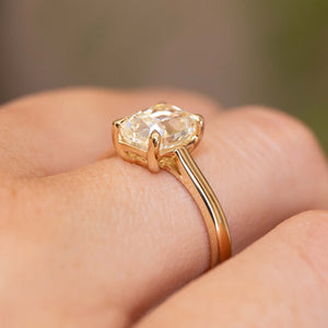 detail of Antique-inspired, cushion-cut diamond solitaire engagement ring in yellow gold worn on a hand and seen from the side to display profile and setting style of ring.