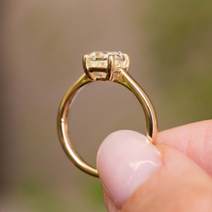 an image of an Antique-inspired, cushion-cut diamond solitaire engagement ring in yellow gold held up to show the profile of the ring against a blurred background