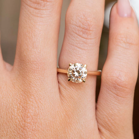 A close-up of a hand wearing a yellow gold solitaire engagement ring with a round brilliant-cut diamond.