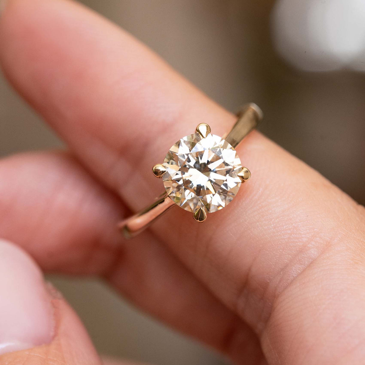 A close-up of a classic solitaire engagement ring with a round brilliant-cut diamond set in a yellow gold band, worn on a person's finger.
