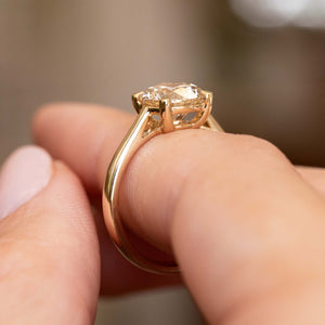 A close-up shot of a gold ring with round-cut light brown diamond being worn on a finger.