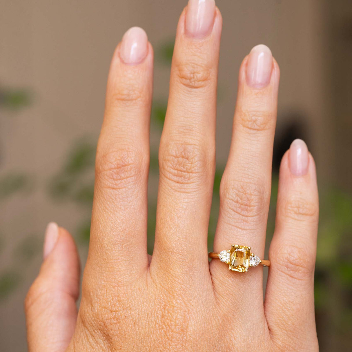 A hand wearing a yellow gold Antique-inspired, Yellow sapphire and diamond three-stone engagement ring held out at a distance to display proportions.
