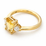 Photo showing the side profile of a yellow gold three-stone engagement ring, inspired by Antique designs and set to centre with a yellow sapphire flanked by two round brilliant-cut diamonds.