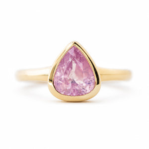 An antique-inspired yellow gold engagement ring featuring pear-cut pink sapphire in a bezel setting, shown against a plain white background.