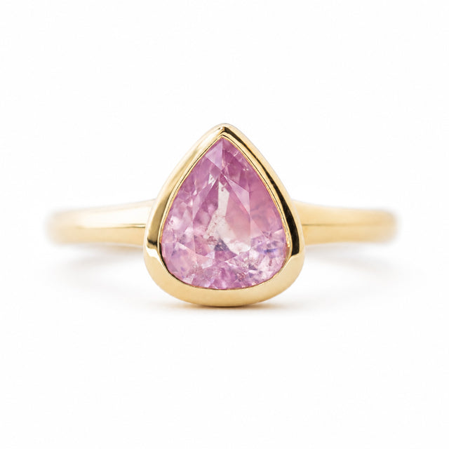An antique-inspired yellow gold engagement ring featuring pear-cut pink sapphire in a bezel setting, shown against a plain white background.