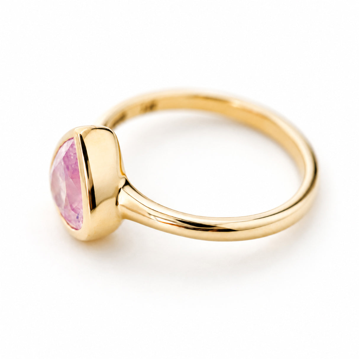 A yellow gold ring with a polished bezel set pink drop-shaped sapphire shown on a clean white background and seen from above to show off the setting style and depth.