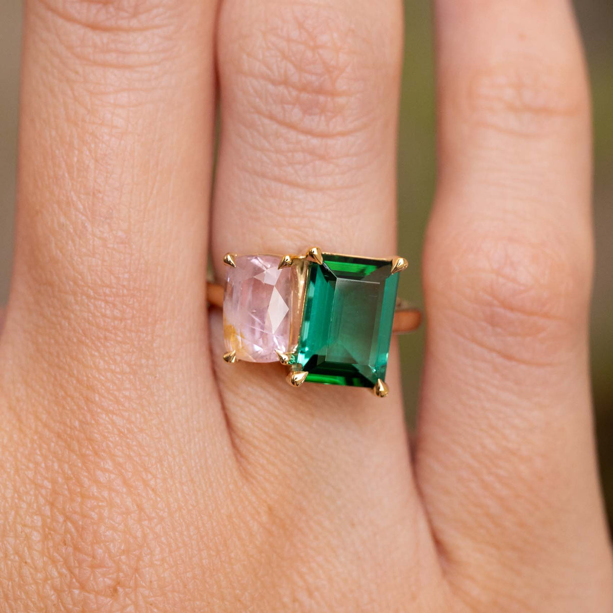 A close-up of a Vintage-inspired, Green tourmaline and pink sapphire Toi et Moi engagement ring worn on the hand