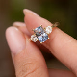 Cushion-cut blue sapphire three-stone ring with brilliant-cut diamond sides and a yellow gold claw setting.
