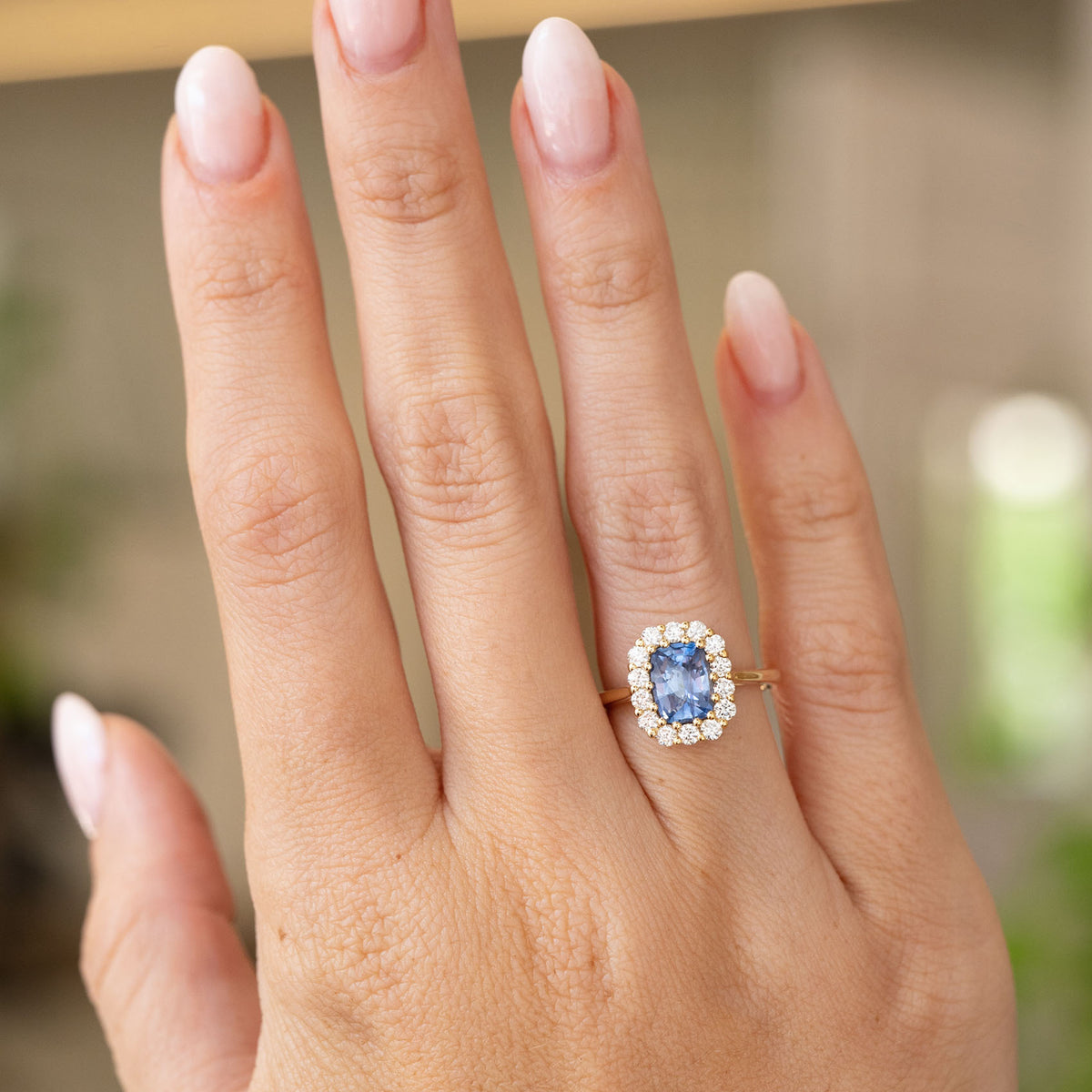 Vintage-inspired cushion-cut blue sapphire and diamond engagement ring worn on the hand, with a slender 14ct yellow gold band.