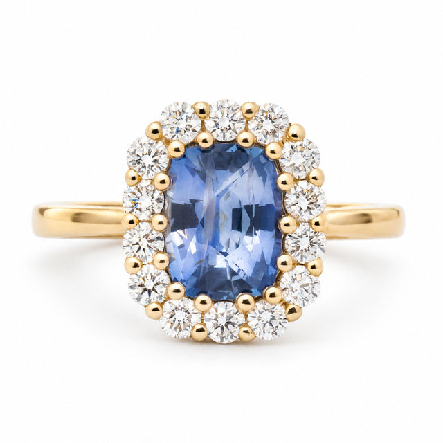 Front view of an antique-inspired cushion-cut blue sapphire engagement ring in 14ct yellow gold, surrounded by a halo of round brilliant-cut diamonds.