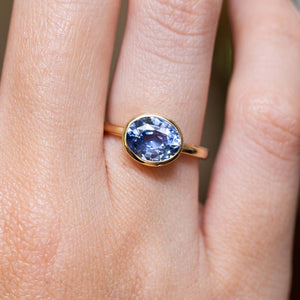 An antique-inspired blue sapphire solitaire ring in yellow gold worn on the finger.