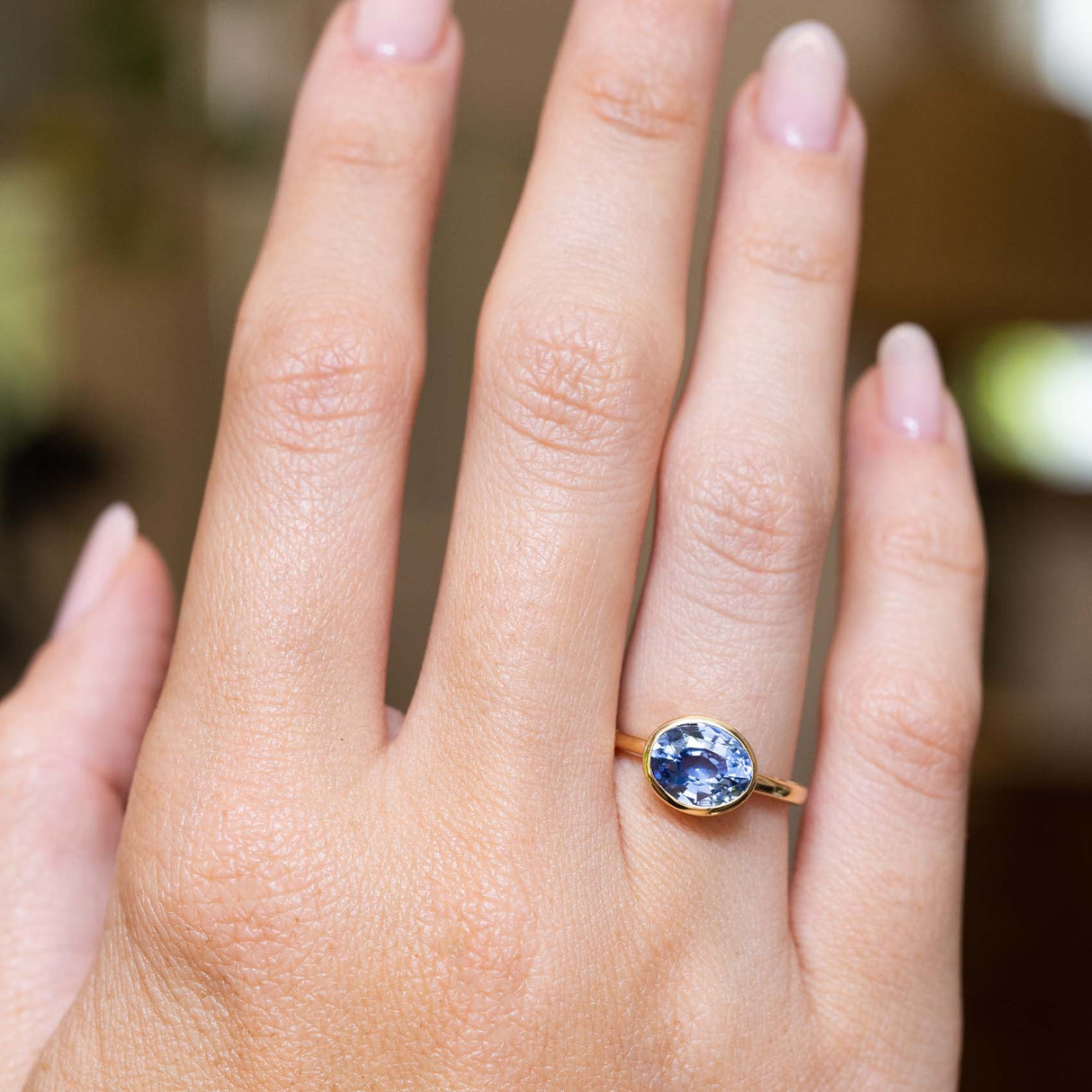 An antique-inspired blue sapphire solitaire engagement ring in yellow gold worn on the hand.