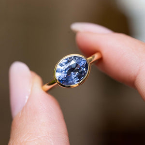 Close detail of an antique-inspired oval-cut blue sapphire solitaire ring in yellow gold held between fingers.