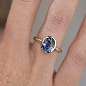 Detailed hand shot of the antique-inspired solitaire, capturing the sapphire’s natural colour variation and sleek gold surround.
