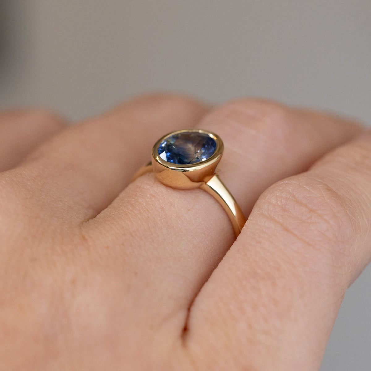 Oblique view of the blue sapphire ring being worn, revealing the gently raised bezel and tapered yellow gold shoulders.