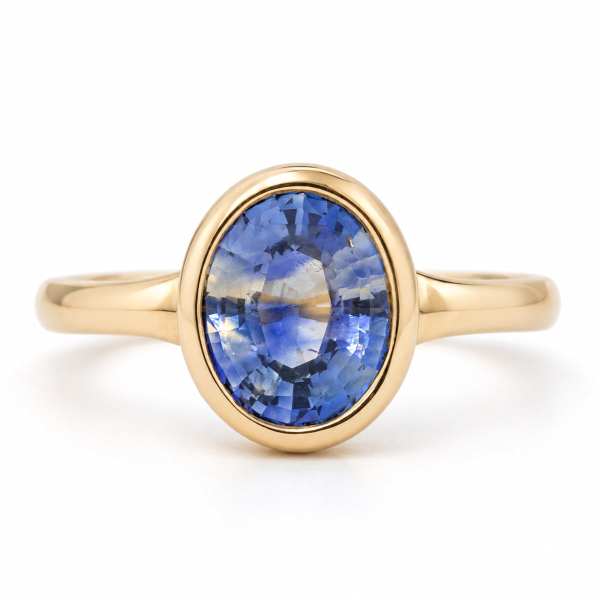 Antique-inspired oval blue sapphire solitaire engagement ring in yellow gold, featuring a smooth rub-over setting and slender band.