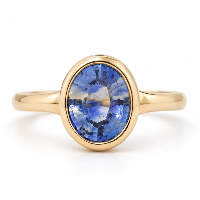 Antique-inspired oval blue sapphire solitaire engagement ring in yellow gold, featuring a smooth rub-over setting and slender band.
