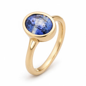 Elevated studio portrait of the blue sapphire ring, revealing its softly rounded gold bezel and clean solitaire silhouette.