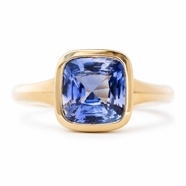 An antique-inspired blue sapphire solitaire ring in yellow gold against a white background.